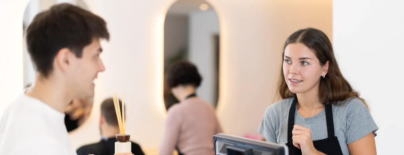 Gast und Mitarbeiterin am Empfangstresen eines Salons