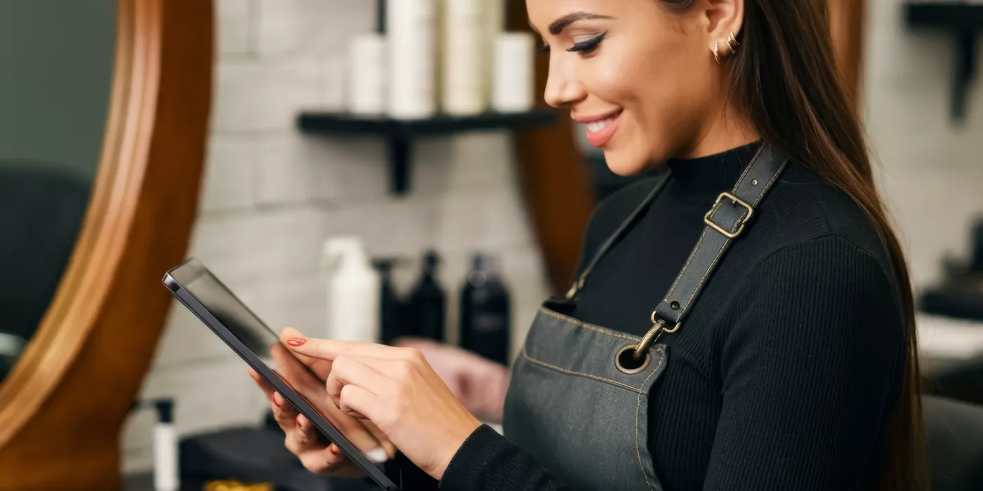 Friseurin sieht am Spiegel auf einem Tablet nach